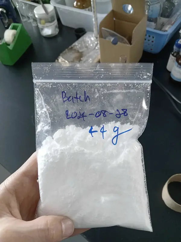 A hand holding a zip bag of white 1-MCP powder in α-cyclodextrin, labelled with its batch date.